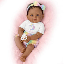 Ashton Drake Ciara baby doll with curly hair, wearing a unicorn-themed shirt and pastel shorts, holding a pacifier.