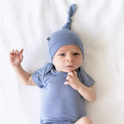 Bamboo baby knotted cap in slate worn by a newborn, laying on a soft white surface, with a thoughtful expression.