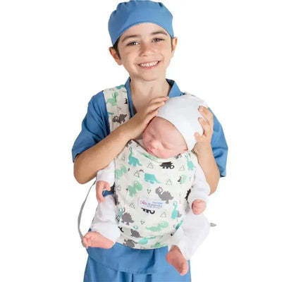 A smiling child in blue scrubs holds a baby doll in a dinosaur-patterned maternity carrier.