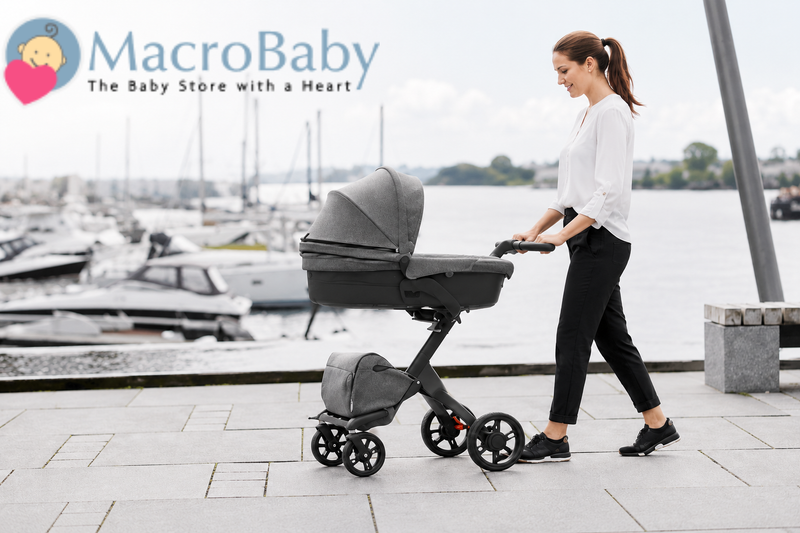 Woman pushing modern baby stroller near waterfront with boats in background