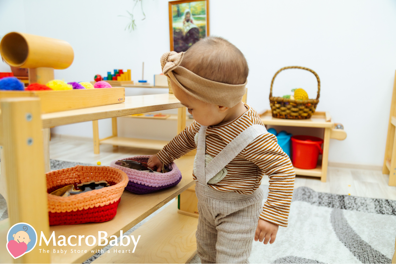 Baby in striped outfit exploring toys on wooden shelf, colorful baskets and Montessori playroom setup