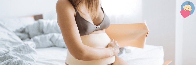Pregnant woman wearing maternity support belt while sitting on bed