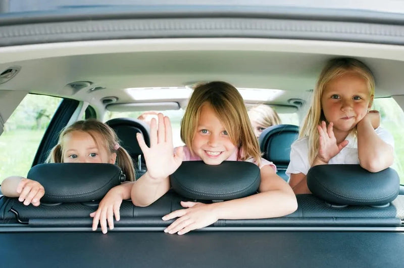 Kids waving from car backseat, showcasing safe family travel with child car seats