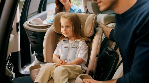 Child in beige car seat with parents nearby, safe and secure for family travel