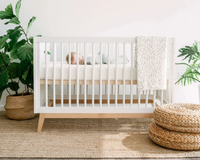 Baby sleeping in white modern crib with speckled blanket, natural rug, and potted plants in nursery
