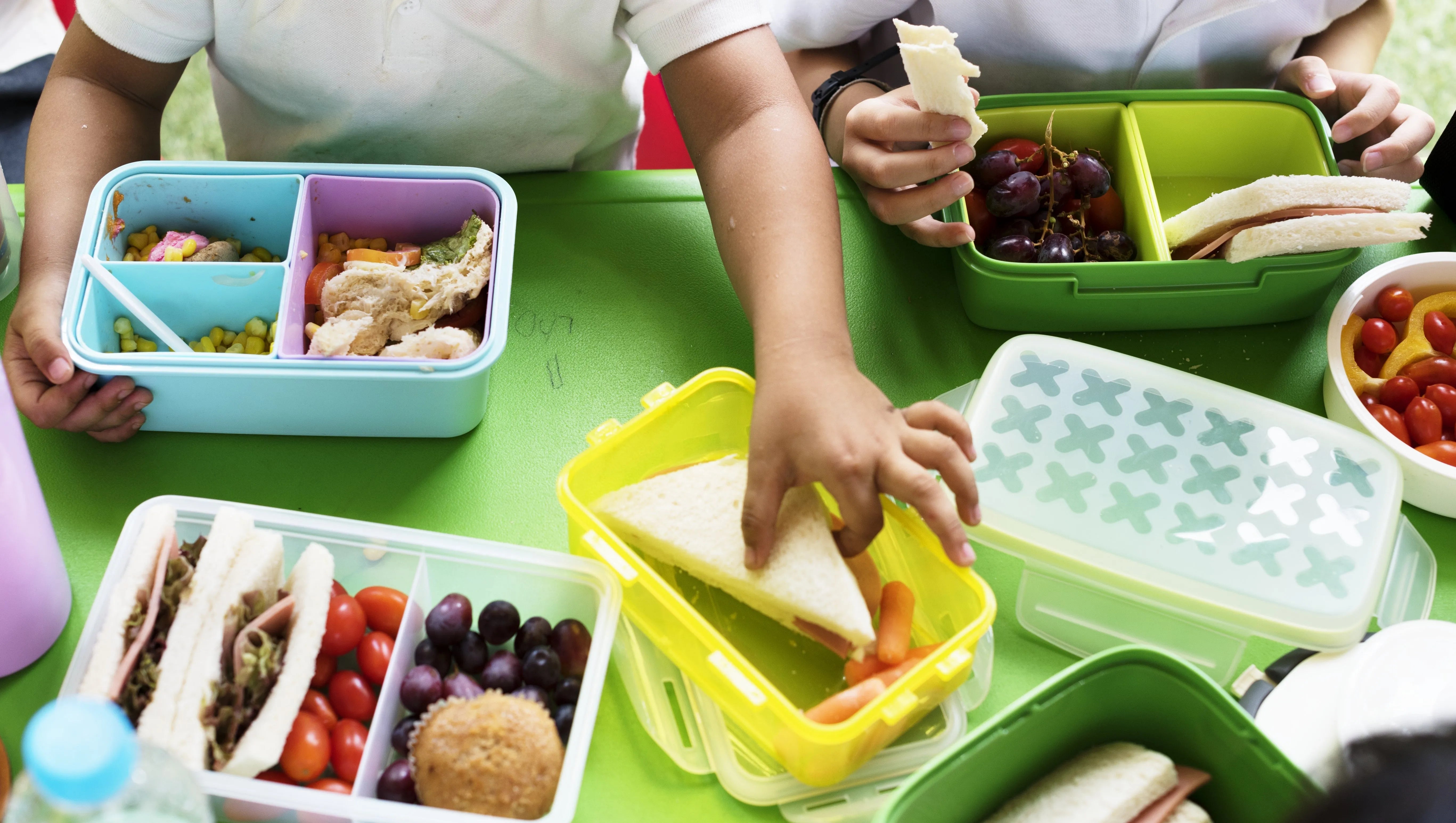 Kids enjoying colorful bento boxes with sandwiches, grapes, and veggies for healthy school lunches.