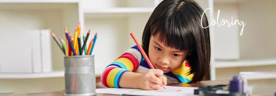 Little girl coloring with crayons at desk, wearing rainbow striped shirt