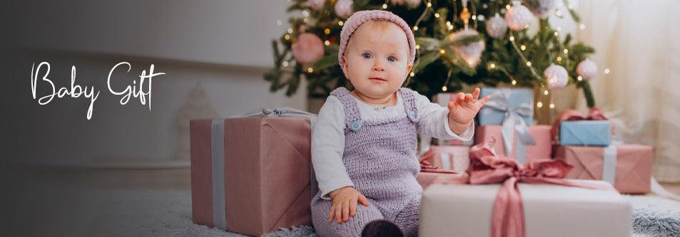Baby in purple knit outfit surrounded by wrapped gifts near Christmas tree, perfect baby gift idea