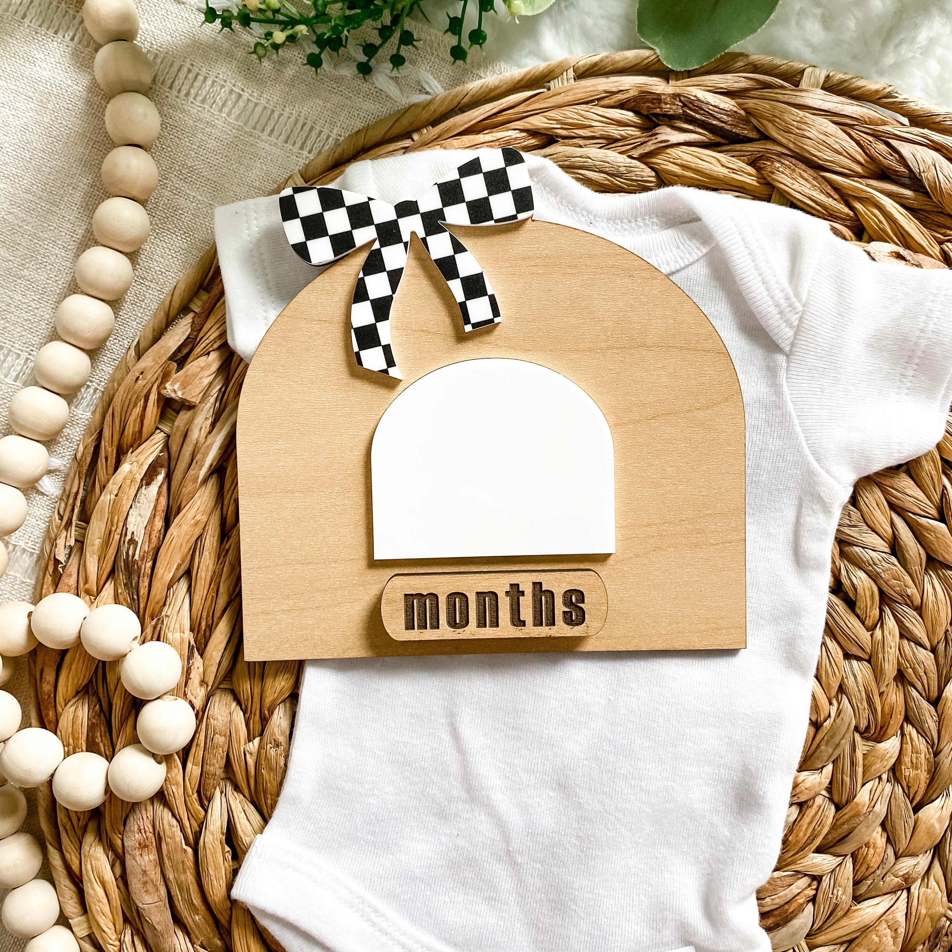 Wooden baby monthly milestone sign with checkered bow, on white onesie, wicker basket, baby clothing