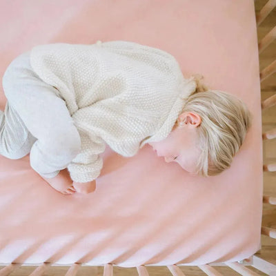 Baby sleeping on a Design Dua waterproof cotton crib sheet in blush pink