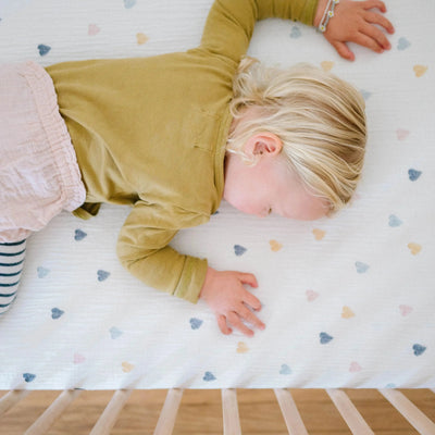 Baby sleeping on a Design Dua waterproof cotton crib sheet with muslin hearts pattern.