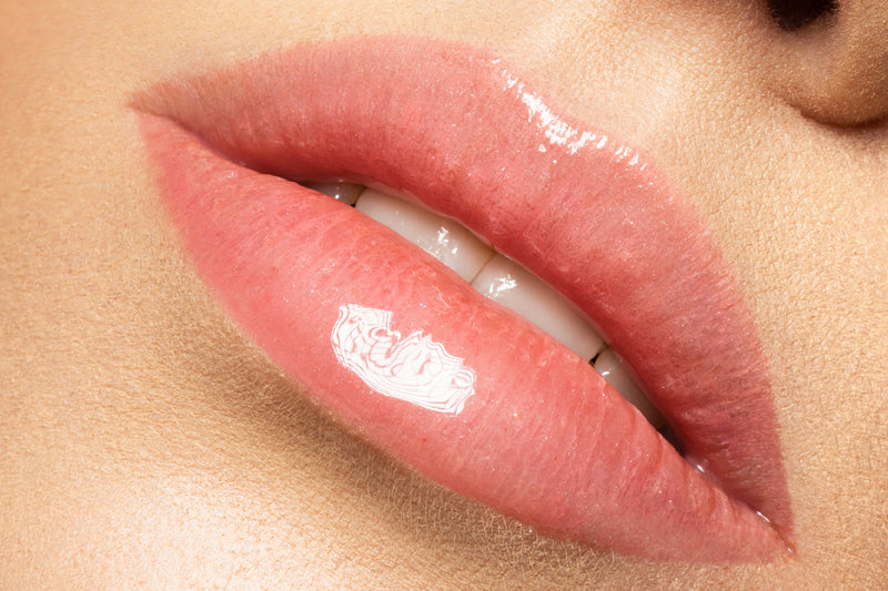 A close-up of a woman's lips with lip gloss, showcasing the results of a lip revitalization procedure. The lips are full, plump, and hydrated, with a natural-looking shine