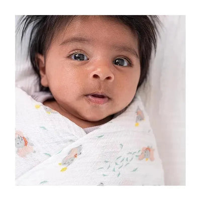 Baby wrapped in a Disney-themed swaddle blanket with pastel animal prints, looking curiously at the camera.