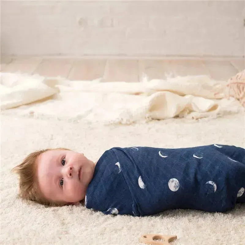 A newborn baby wrapped in a navy blue swaddle with moon patterns, lying on a soft, textured surface.