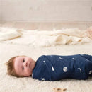 A newborn baby wrapped in a navy blue swaddle with moon patterns, lying on a soft, textured surface.