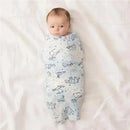 A wrapped baby lying on a white surface, swaddled in a light blue Aden + Anais fabric featuring stargaze designs.