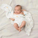 Smiling baby wrapped in Aden + Anais Stargaze swaddles, featuring a soft, starry design with colorful dots.