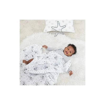 A baby lies on a soft surface, wrapped in a white muslin swaddle with a Mickey mouse stargazer print, smiling.