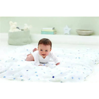 Baby lying on a polka-dotted swaddle blanket, smiling, with soft toys and a star decoration in the background.