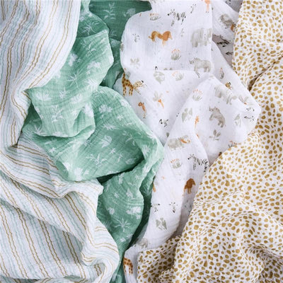 Four cotton muslin swaddles featuring various designs: giraffes, lions, and plants in pastel colors and patterns.