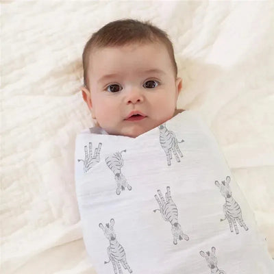 Baby swaddled in an Aden + Anais muslin blanket featuring a grey zebra print, resting on a soft surface.