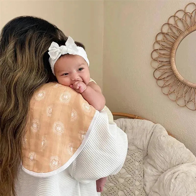 A baby in a soft, patterned burpy bib is being held by a caregiver, both smiling and content in a cozy setting.