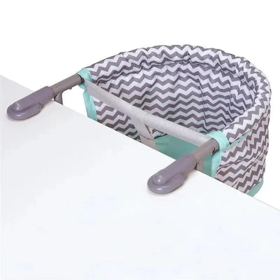 Zigzag patterned feeding seat designed to attach to a table, featuring a padded edge and plastic clips for secure fastening.