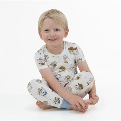 Child wearing a short sleeve loungewear set featuring playful cowdog illustrations, smiling while seated.