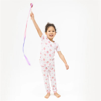 Smiling girl wearing a pink floral short sleeve loungewear set, playing with a colorful ribbon in a bright setting.