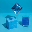 Blue cotton candy drink glitter bombs being added to a blue drink, with decorative balloons and packaging nearby.