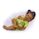 Realistic Ashton Drake Alexis Baby Doll wearing a green dress with a flower, lying on a light purple surface, smiling.