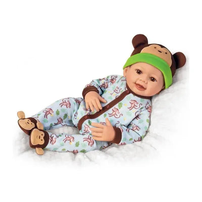 Lifelike baby doll named Lucas dressed in monkey-themed pajamas, wearing a green monkey hat, with a playful expression.