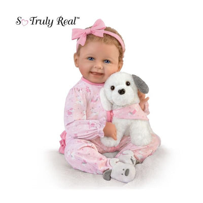 Baby girl doll Layla in pink pajamas holds a plush puppy, smiling with a pink bow in her hair.