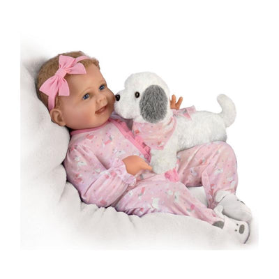 Lifelike baby girl doll in pink pajamas with a bow, cuddling a small stuffed puppy.