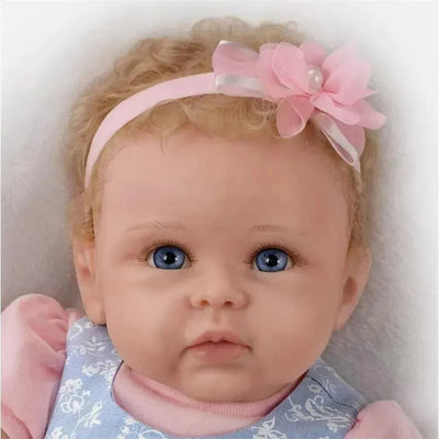 Baby doll with blue eyes, curly hair, and a pink headband adorned with a flower, wearing a light blue dress.