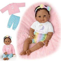 Ashton Drake One Of A Kind Ciara baby doll wearing a rainbow outfit and a headband, next to a pink cardigan and pants.