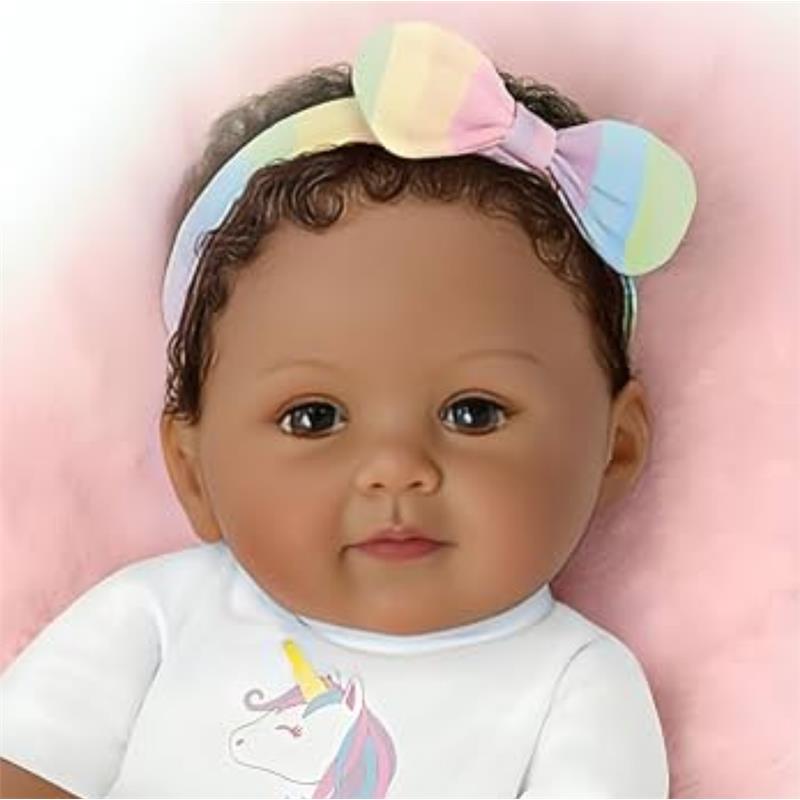Ashton Drake Ciara baby doll with soft curly hair, wearing a unicorn-themed onesie and a colorful bow headband.