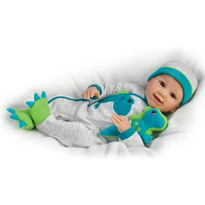 Ashton Drake Ryan And Rex Baby Boy Doll wearing a gray onesie with colorful dinosaur details, smiling while holding a plush toy.
