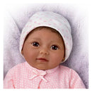 Lifelike doll named Kiara, wearing a pink polka-dot outfit and a white hat, resting on a soft blanket.