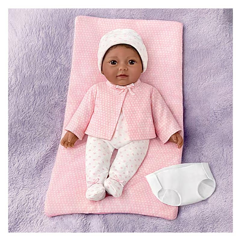 Lifelike Ashton Drake Tiny Miracles doll, 10 Little Kiara, dressed in pink outfit with bow, resting on a pink blanket with a diaper beside.