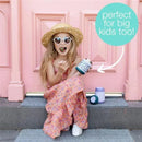 Girl in a pink dress and straw hat eating from a B.box Friendly Fox insulated food jar, with a playful expression and colorful door background.