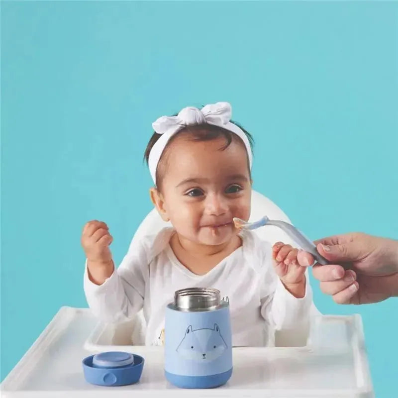 Smiling baby in a high chair enjoys food from a blue B.box Friendly Fox insulated food jar with a spoon.
