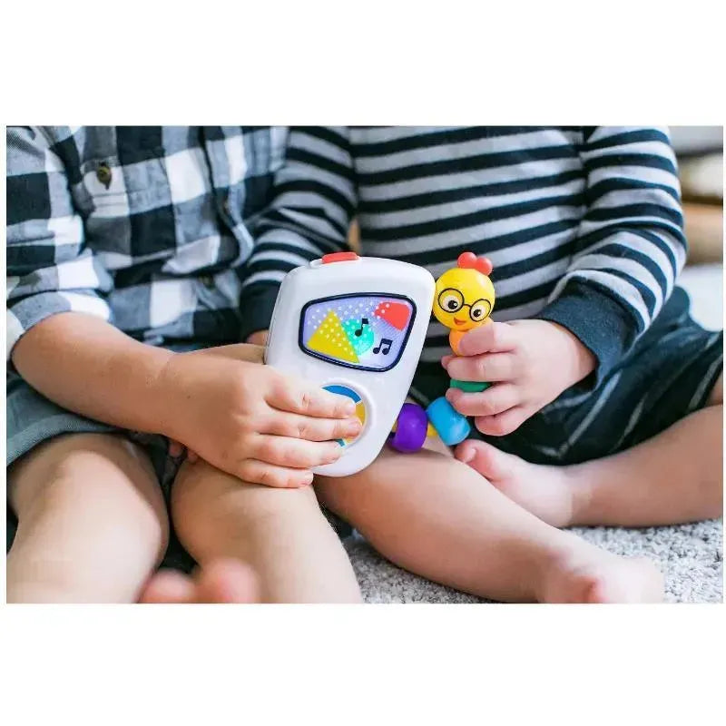 Two children are sitting on a carpet, one holding a Baby Einstein Take Along Tunes Musical Toy with buttons and colorful designs, while the other child plays with a yellow chick toy.