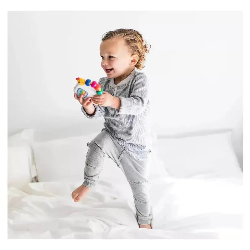 Toddler joyfully playing with the Baby Einstein Take Along Tunes Musical Toy while standing on a bed.