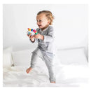 Toddler joyfully playing with the Baby Einstein Take Along Tunes Musical Toy while standing on a bed.