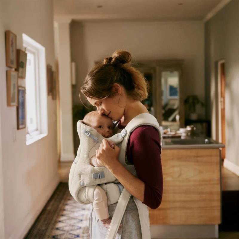 Mother using a Babybjorn Baby Carrier Hold Mesh in black, gently kissing her baby, in a cozy indoor setting.