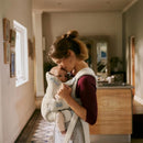 Mother using a Babybjorn Baby Carrier Hold Mesh in black, gently kissing her baby, in a cozy indoor setting.
