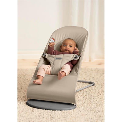 Babybjorn Bouncer Balance Soft in sand gray, featuring a seated baby wearing pastel pants and a cozy sweater, smiling and playing.