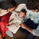 Light green Babybjorn Bouncer Begin features a baby in a striped outfit, gently held by parents sitting beside.