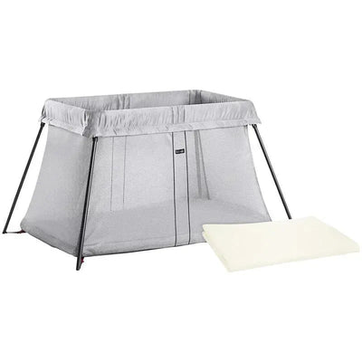Travel crib in silver with mesh sides, bundled with a white fitted sheet placed beside it.